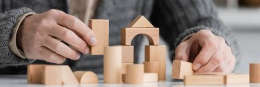 partial view of senior man with alzhemeirs disease playing with wooden blocks at home, banner