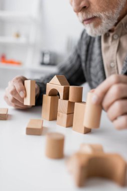 partial view of man with alzheimer disease playing building blocks game on blurred foreground