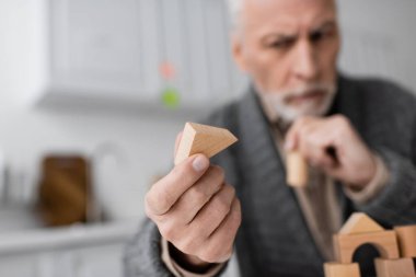 selective focus of wooden block in hand of senior man with alzheimer syndrome on blurred background