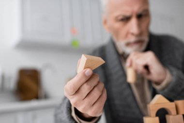 selective focus of wooden block in hand of senior man with alzheimer syndrome on blurred background clipart