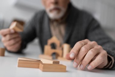 partial view of aged man sick on alzheimer syndrome playing building blocks game on blurred background