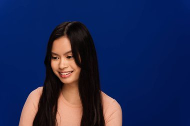 Smiling asian woman looking away isolated on blue 