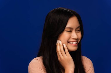 Positive asian model closing eyes isolated on blue 