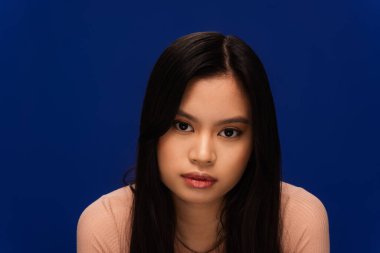 Portrait of asian woman looking at camera isolated on blue 