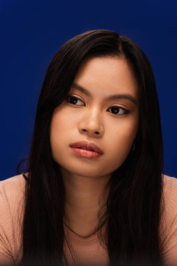 Portrait of young asian woman with natural makeup looking away isolated on blue 