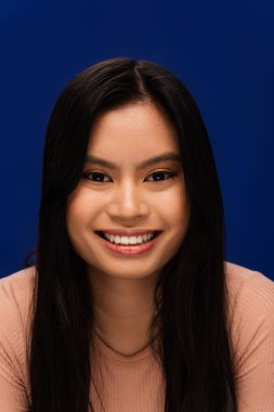Portrait of cheerful asian woman looking at camera isolated on blue 