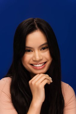 Portrait of happy young asian woman looking at camera isolated on blue 