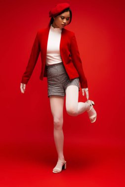Full length of asian woman in jacket and shorts standing on red background 