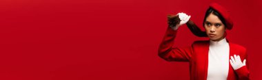 Stylish asian model in white gloves touching hair isolated on red, banner 