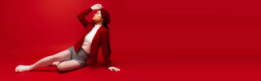 Side view of fashionable asian mode posing while sitting on red background, banner 