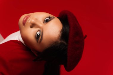 Portrait of asian model in beret looking at camera isolated on red 