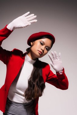 Fashionable asian model with makeup and white gloves posing isolated on grey 