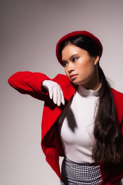 Asian model with makeup and in red jacket posing isolated on grey 