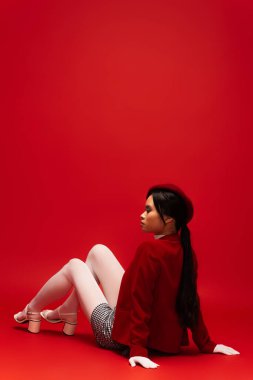 Side view of fashionable asian woman sitting on red background 