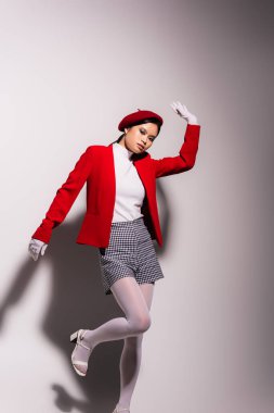 Trendy asian woman in red and white outfit posing on grey background with shadow 