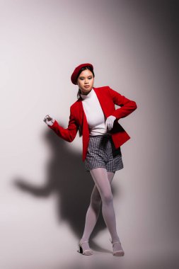 Trendy asian model in white gloves and red jacket posing on grey background with shadow  clipart