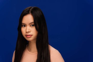 Pretty young asian woman with perfect skin looking at camera isolated on navy blue