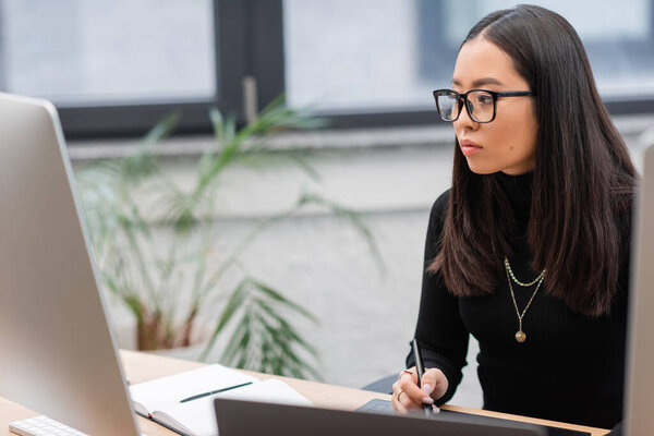 Азиатский дизайнер интерьеров с помощью графического планшета возле компьютеров в офисе 