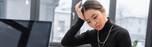 Напряженный азиатский дизайнер интерьеров, стоящий рядом с монитором компьютера в офисе, баннер 