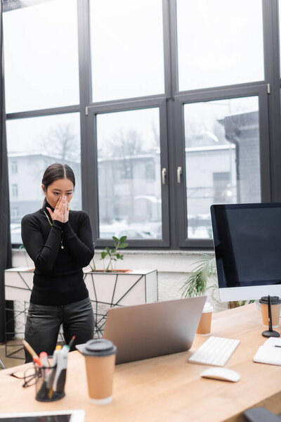 Стресс азиатский дизайнер интерьера стоя возле ноутбука на столе в студии 