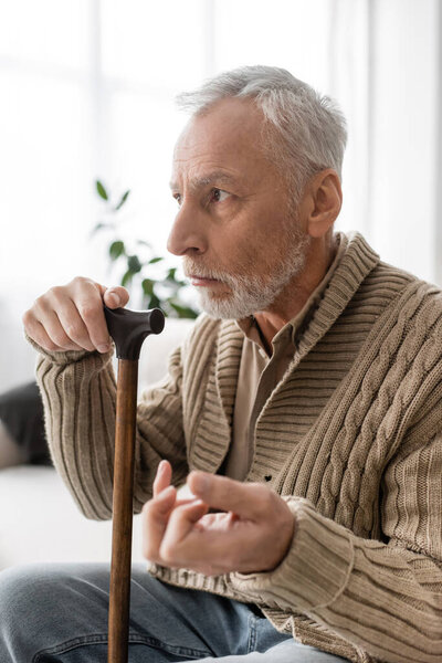 depressed man with parkinsonian syndrome sitting with walking cane and looking away at home