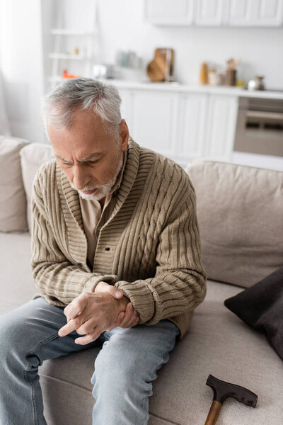 anxious man with parkinson disease and hands tremor sitting on couch at home