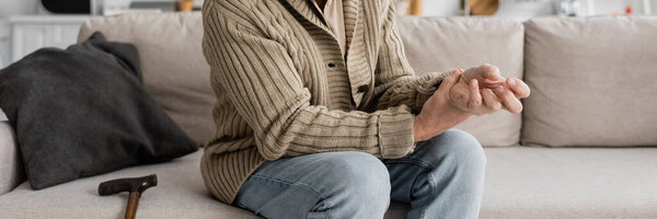 partial view of aged man with trembling hands suffering from parkinsonian syndrome while sitting on sofa, banner
