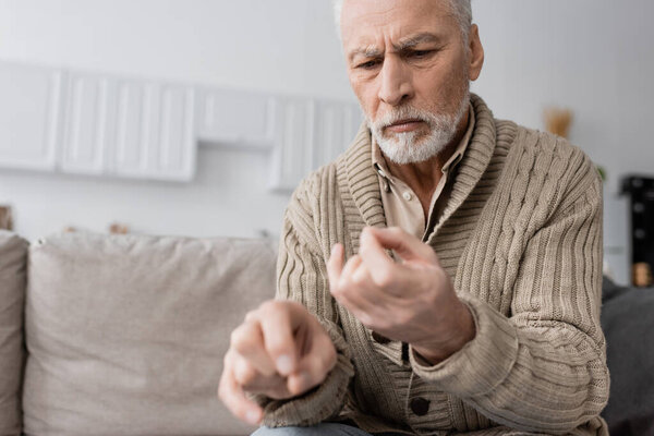 worried senior man suffering from parkinsonian syndrome and looking at trembling hands on blurred foreground