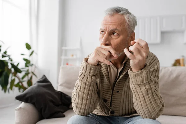 depressed and anxious man with parkinson disease holding trembling hands near face and looking away at home