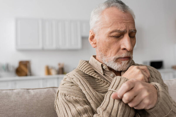depressed senior man with parkinson disease sitting with closed eyes at home