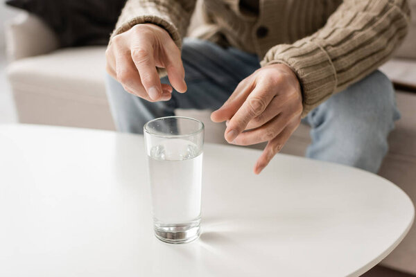 cropped view of man with parkinson disease and trembling hands sitting near glass of water at home