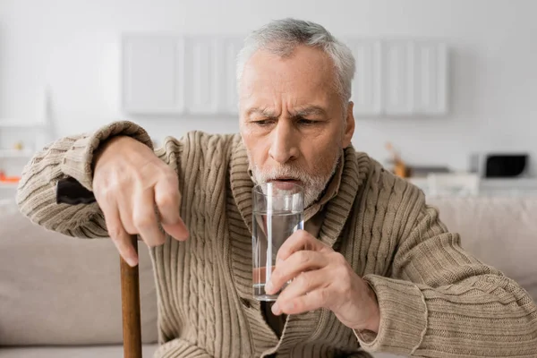 tense man suffering from parkinson syndrome and holding glass of water in trembling hand