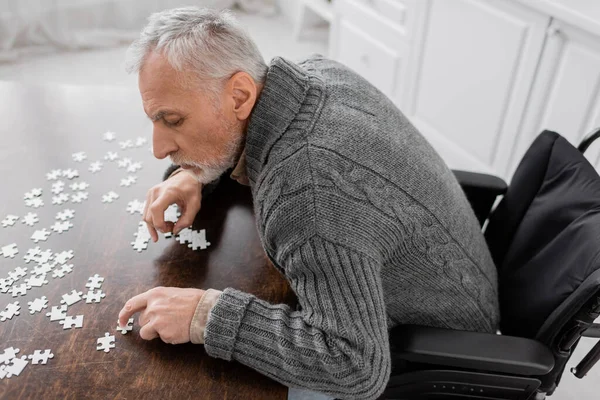 high angle view of man with parkinson disease sitting in wheelchair near elements of jigsaw puzzle