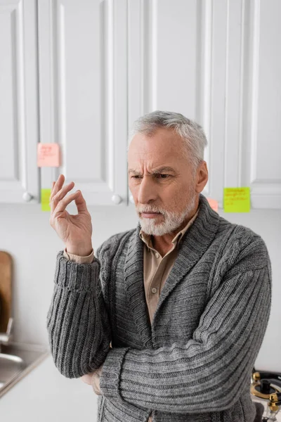 thoughtful man with alzheimer disease standing near blurred sticky notes in kitchen