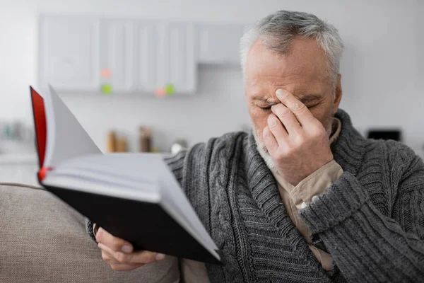 stock image depressed man with alzheimer syndrome sitting with closed eyes and blurred notebook at home