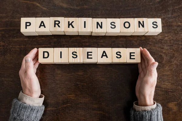 木の表面にパーキンソン病の文字が書かれたブロックの近くにクロップドシニアの男のトップビュー — ストック写真