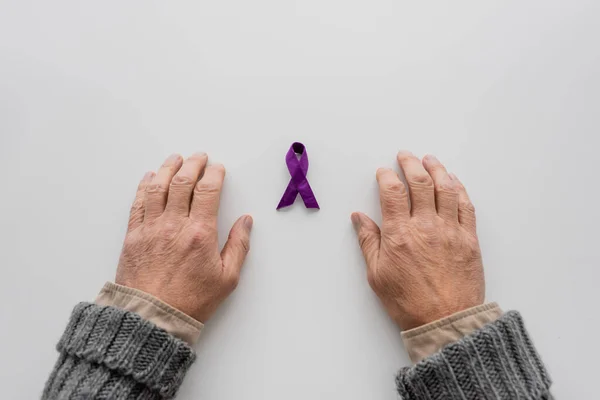 白い表面に紫色のリボンの近くにアルツハイマー病の老人の手のトップビュー — ストック写真