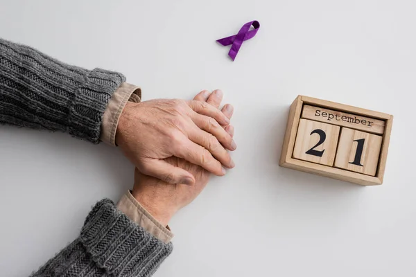 stock image top view of cropped man with alzheimer syndrome near purple ribbon and wooden calendar with september 21 date on white surface