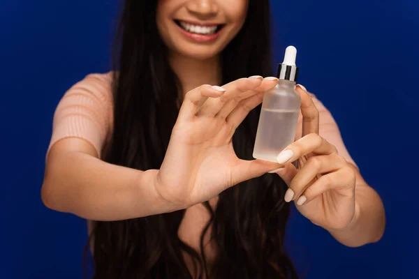 Stock image Cropped view of blurred woman holding bottle with cosmetic serum isolated on blue 
