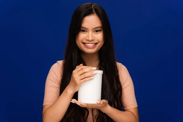 stock image Brunette asian woman holding jar with cosmetic product isolated on blue 