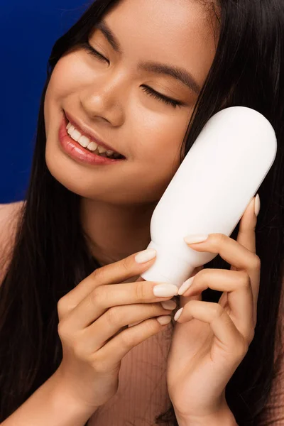 stock image Portrait of smiling asian woman holding body lotion isolated on blue 