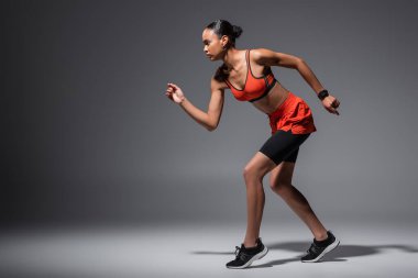 full length of young african american woman in sneakers running on grey 