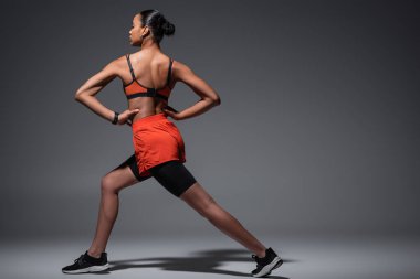 full length of young african american woman in sportswear and sneakers exercising with hands on hips on grey 