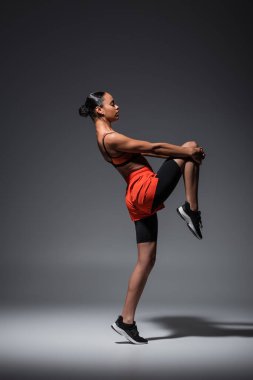 full length of sportive african american woman in sneakers training on grey 