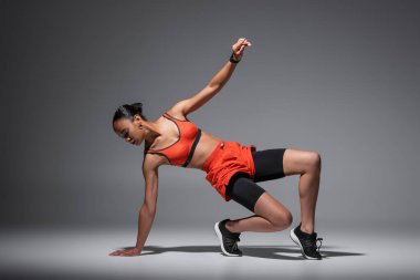 full length of strong and sportive african american woman working out on grey background 