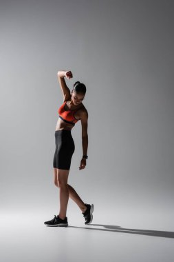 full length of brunette african american woman posing in sports bra and shorts on grey 