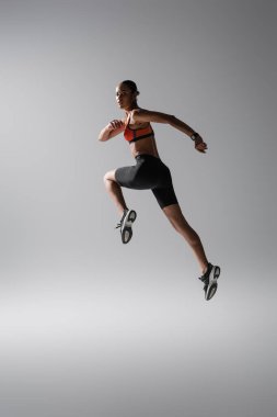 full length of brunette african american woman levitating during work out on grey