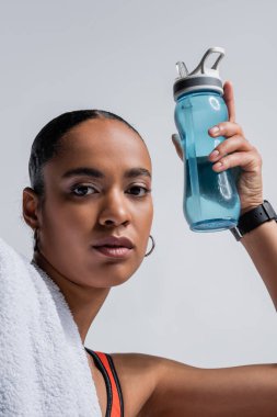 brunette african american woman in sports bra holding sports bottle with water isolated on grey 