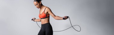 sportive african american woman exercising with skipping rope on grey background, banner 