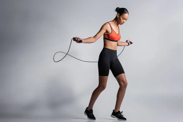 Stock image full length of sportive african american woman exercising with skipping rope on grey 